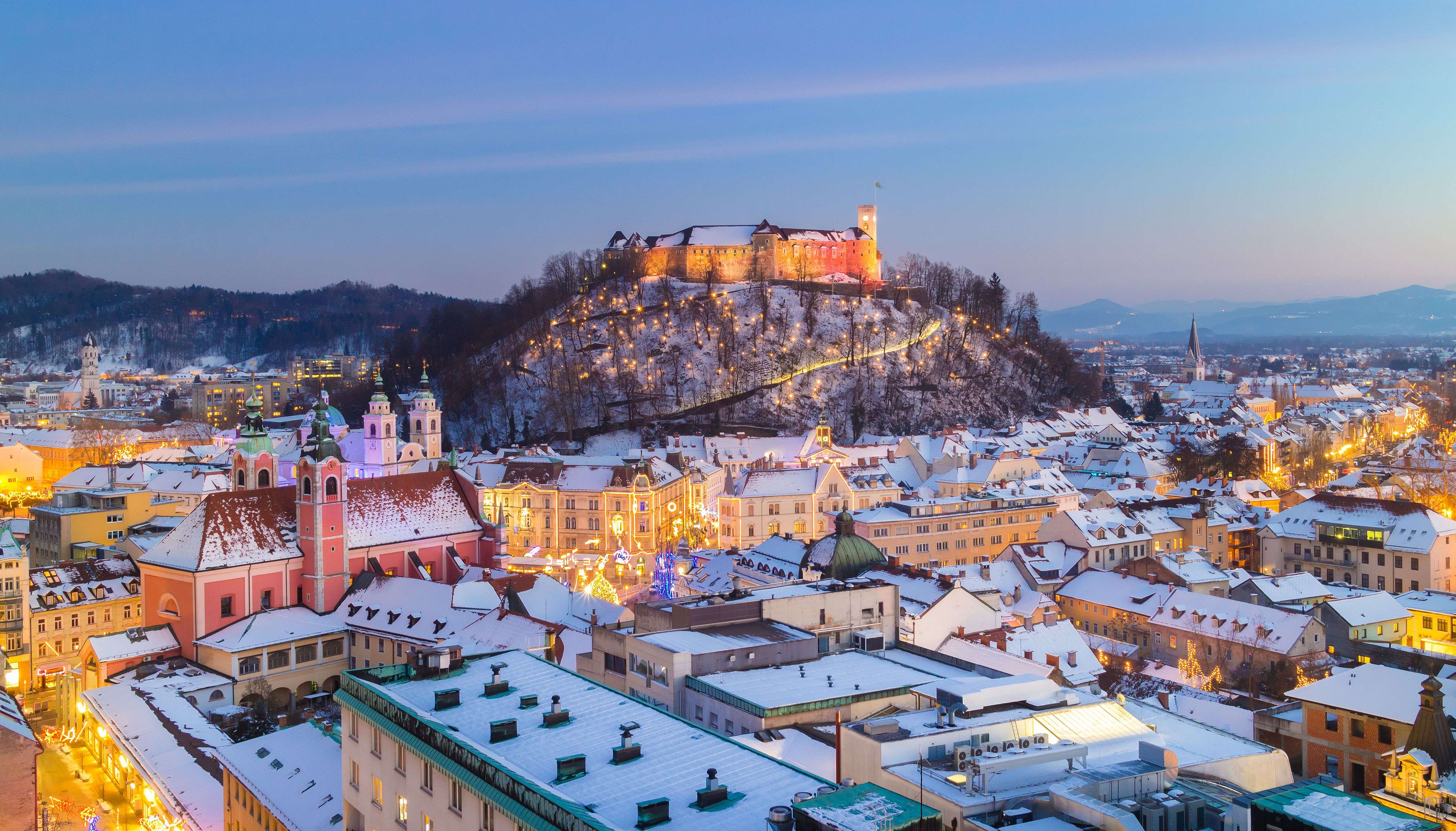 Illuminated castle overlooking snowy city rooftops at twilight