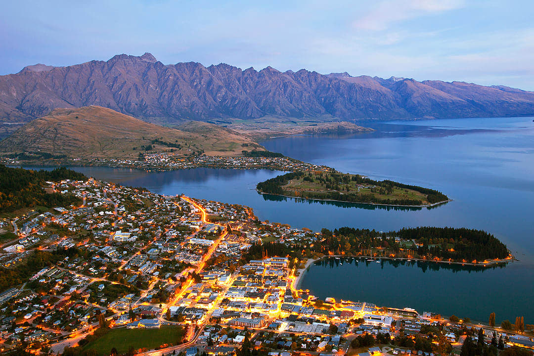 Lights shimmer as Queenstown rests beneath towering peaks and calm waters.