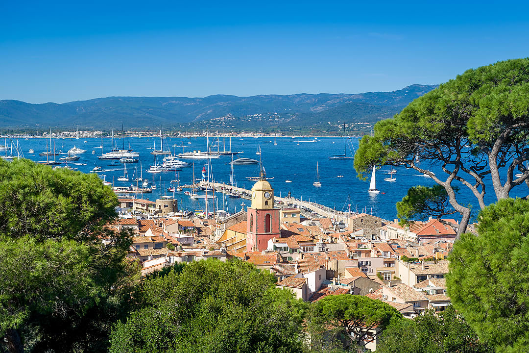 Scenic view of Saint-Tropez harbor, France, with luxury yachts, colorful rooftops, and blue Mediterranean