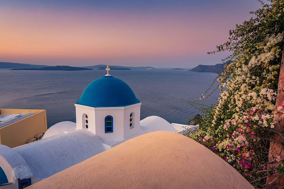 The whitewashed buildings of Oia overlook the deep blue sea, glowing in the sunset’s light.
