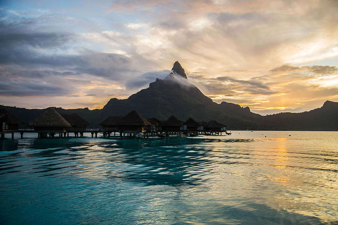 Sun setting behind Mount Otemanu, with overwater bungalows on the lagoon.