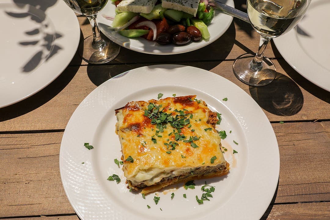 Plate of baked Greek moussaka served with salad and wine.
