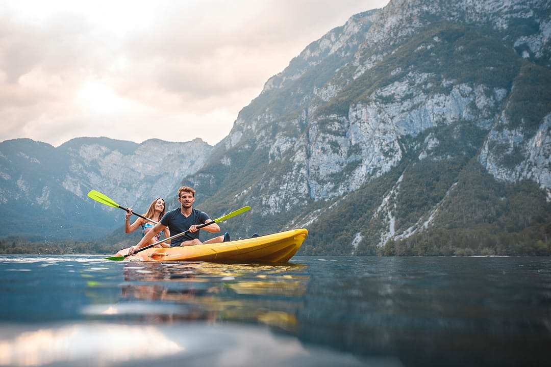 Couple kayaking on calm alpine lake near mountains