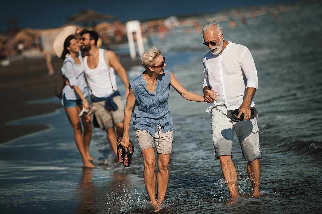 Multi-generational family walking along a sun-drenched beach in shallow water.