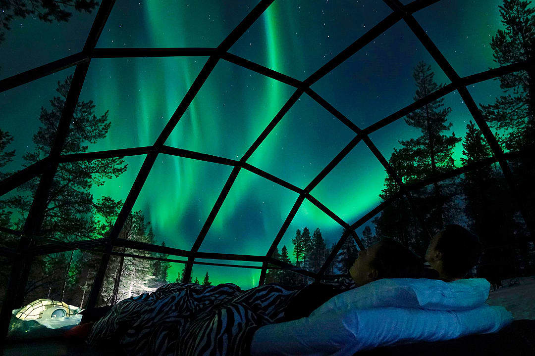Couple watching the northern lights from inside a glass igloo in Finland