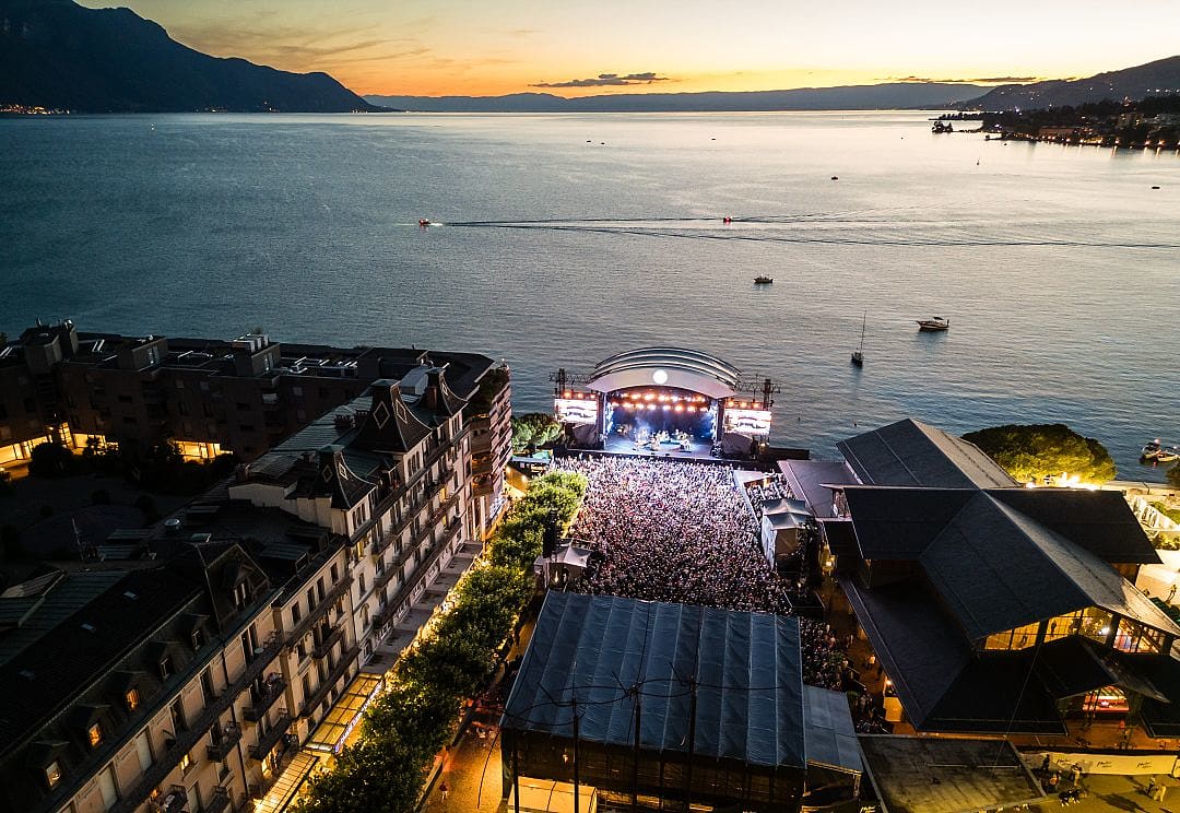 Sunset over Lake Geneva at the Montreux Jazz Festival, vibrant crowd, scenic mountains, and water views.