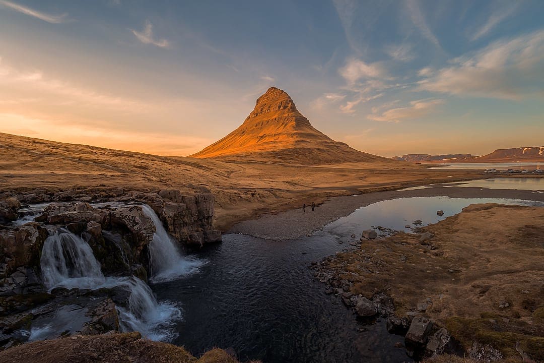 Golden sun shining on Kirkjufell Mountain, with waterfalls in the foreground.