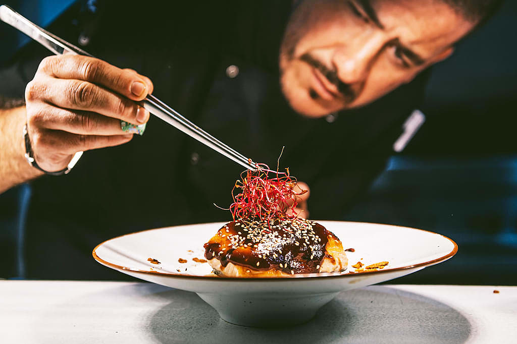 Chef garnishing a gourmet dish with tweezers in a fine dining restaurant kitchen