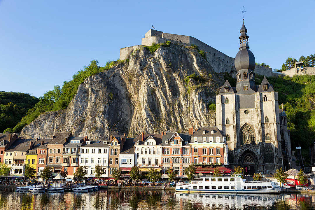 Colorful historic buildings along a river with a steep cliff.