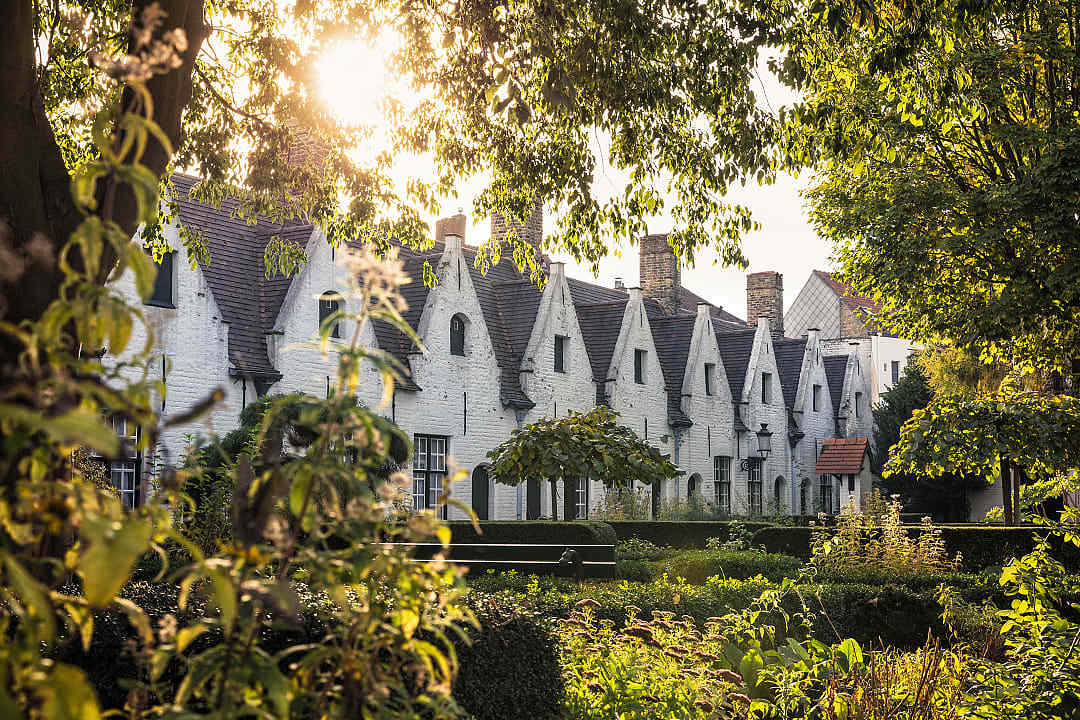 White gabled almshouses surrounded by gardens in the historic center of Bruges, Belgium.
