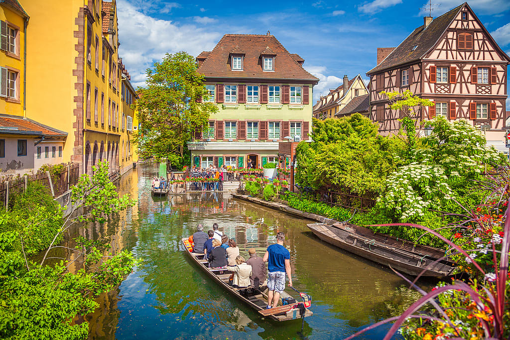 Senior tourists on boat ride in canal with traditional colorful houses in Colmar, France
