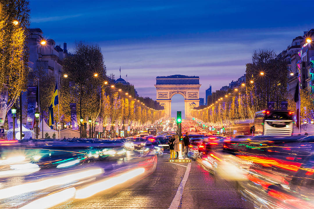 Champs-Élysées in Paris at night with festive Christmas lights leading to the Arc de Triomphe, vibrant traffic trails creating a holiday scene