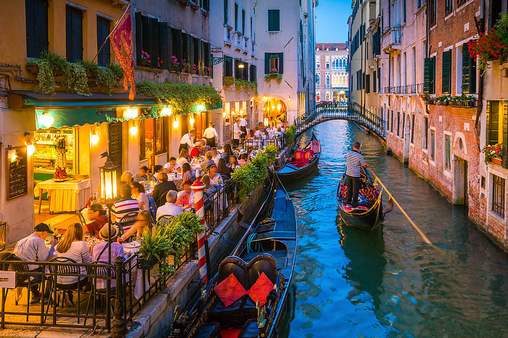 Gondolas passing by a restaurant on a canal in Venice, Italy at night
