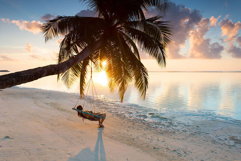 Woman lounging in a hanging chair watching the sunset in the Maldives