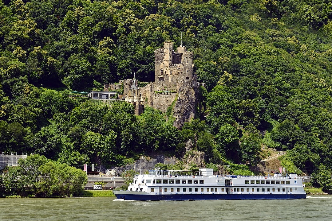 Cruise ship and Castle Rheinstein on a rocky cliff overlooking the Rhine River in Germany.