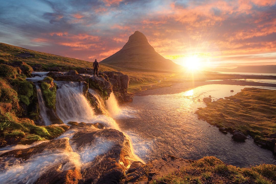 Silhouette of man watching the sunset over Kirkjufellsfoss with Kirkjufell mountain in Iceland