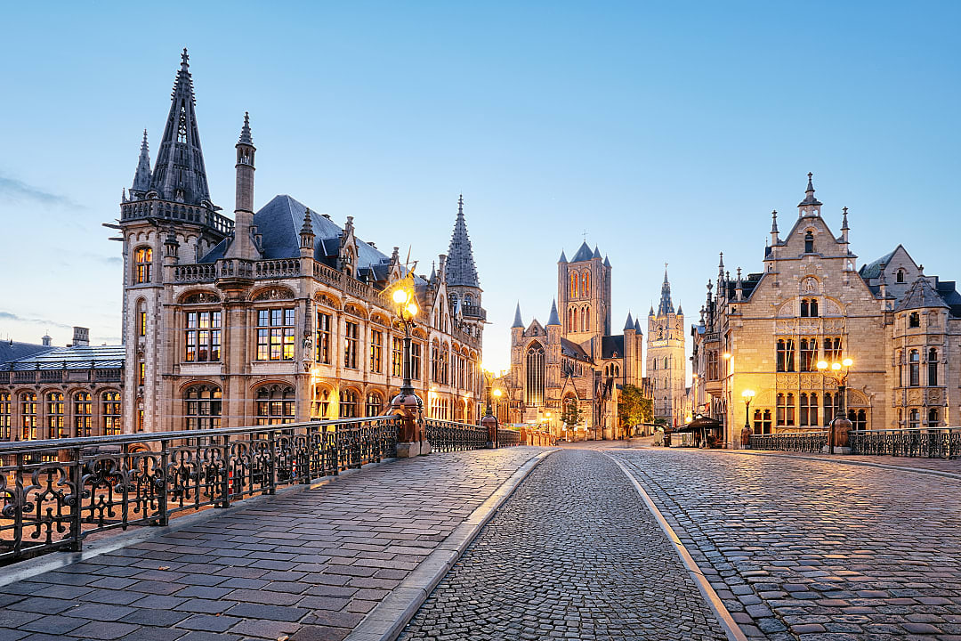 A cobblestone bridge in the medieval center of Ghent, Belgium, surrounded by Gothic and Flemish-style buildings.