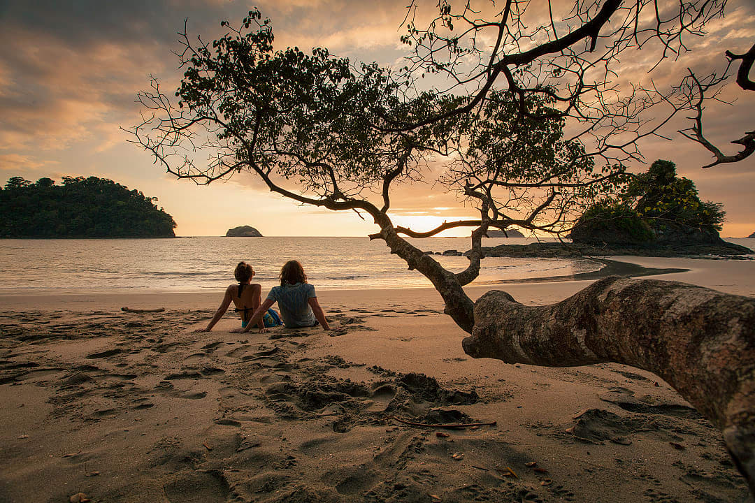 Couple sitting on the beach watching the sunset in Manuel Antonio National Park