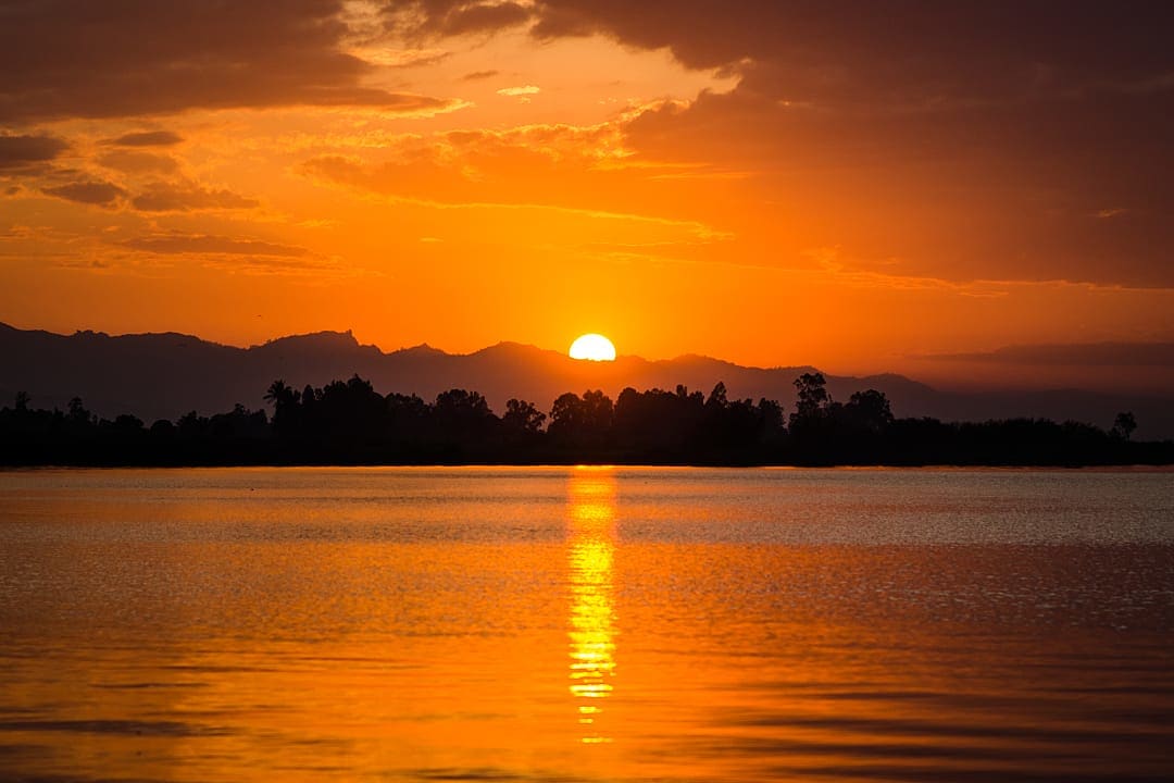 Golden sunset over a calm lake with silhouetted trees and mountains in the background