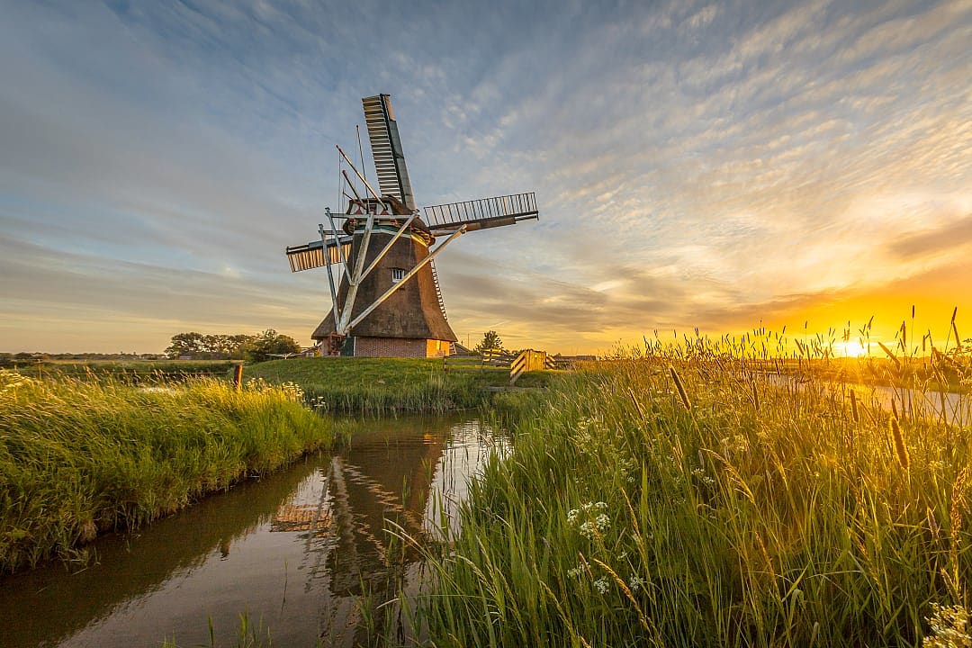 Kinderdijk’s windmill stands tall, reflecting in the peaceful sunset waters.