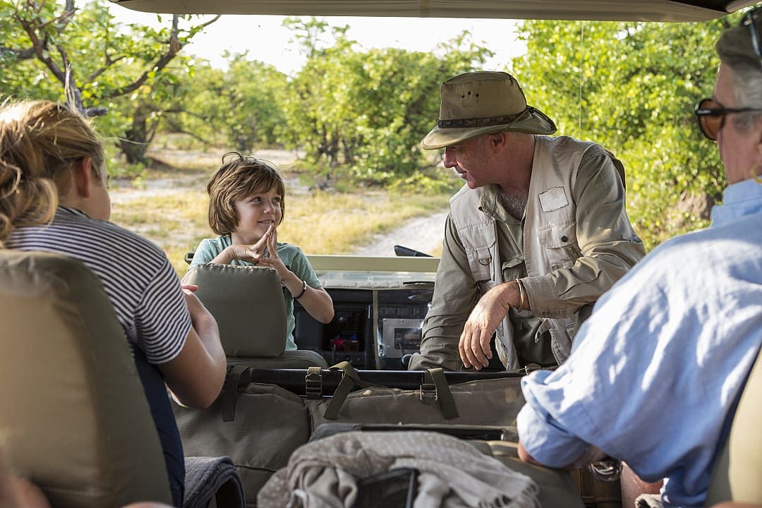 A safari guide speaking with a family inside an open vehicle, sharing knowledge and creating a personal connection during a wildlife adventure.