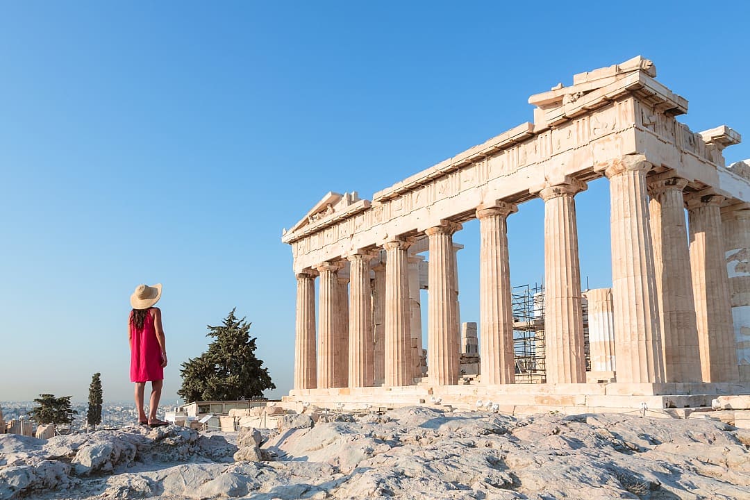 A woman admires the Parthenon’s ancient columns under the clear sky.