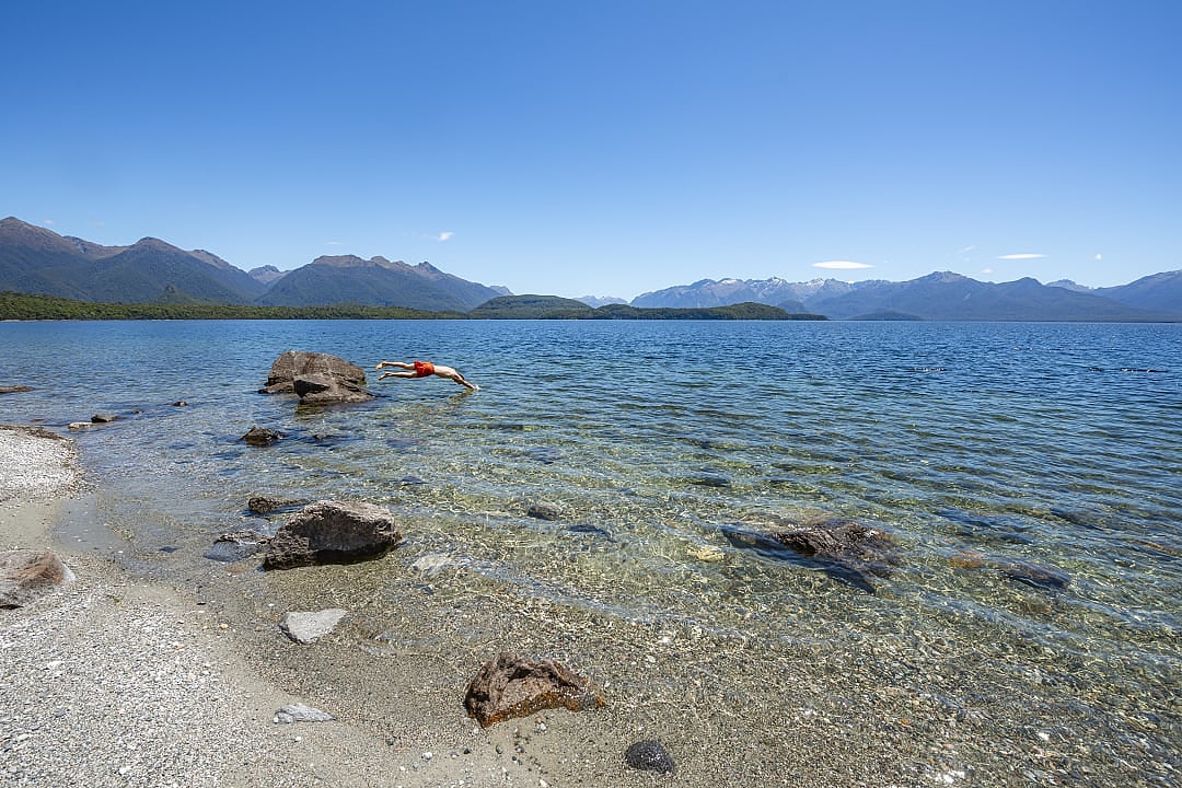 Clear waters, mountain views, swimmer diving in Lake Manapouri.