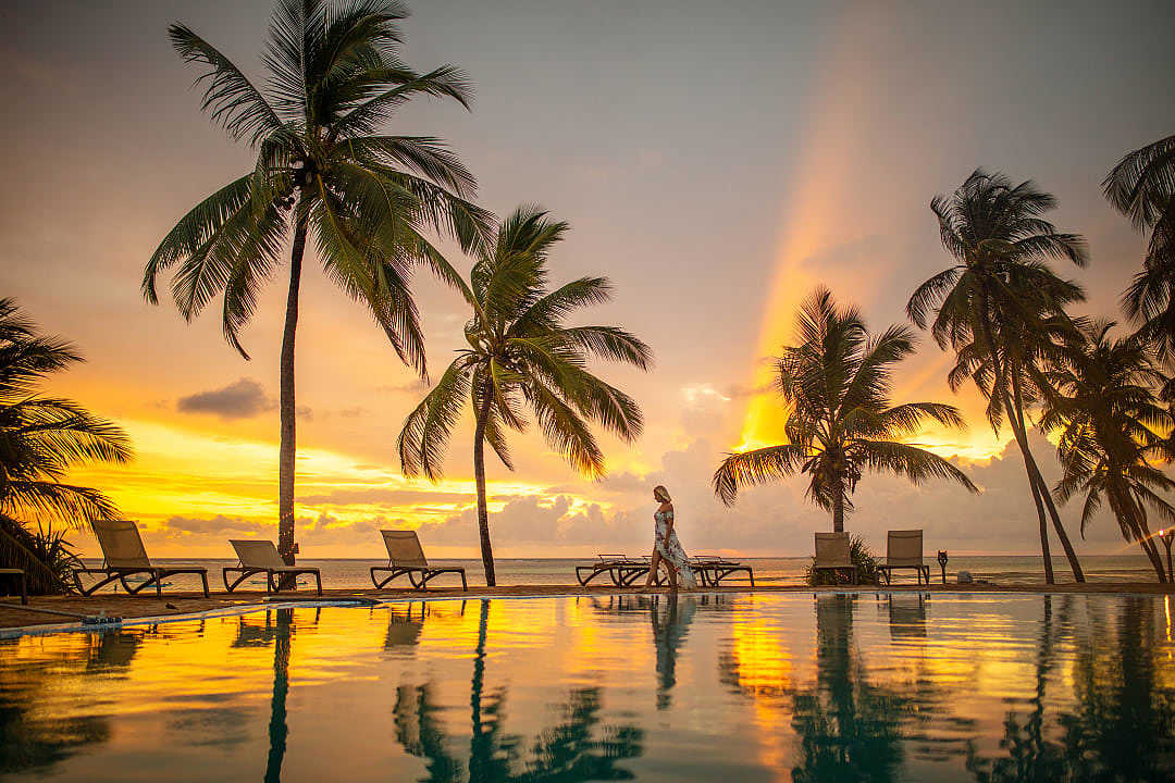 A woman walks by the beachside hotel pool area of a luxury hotel in Zanzibar, enjoying the peaceful ocean view at sunset.