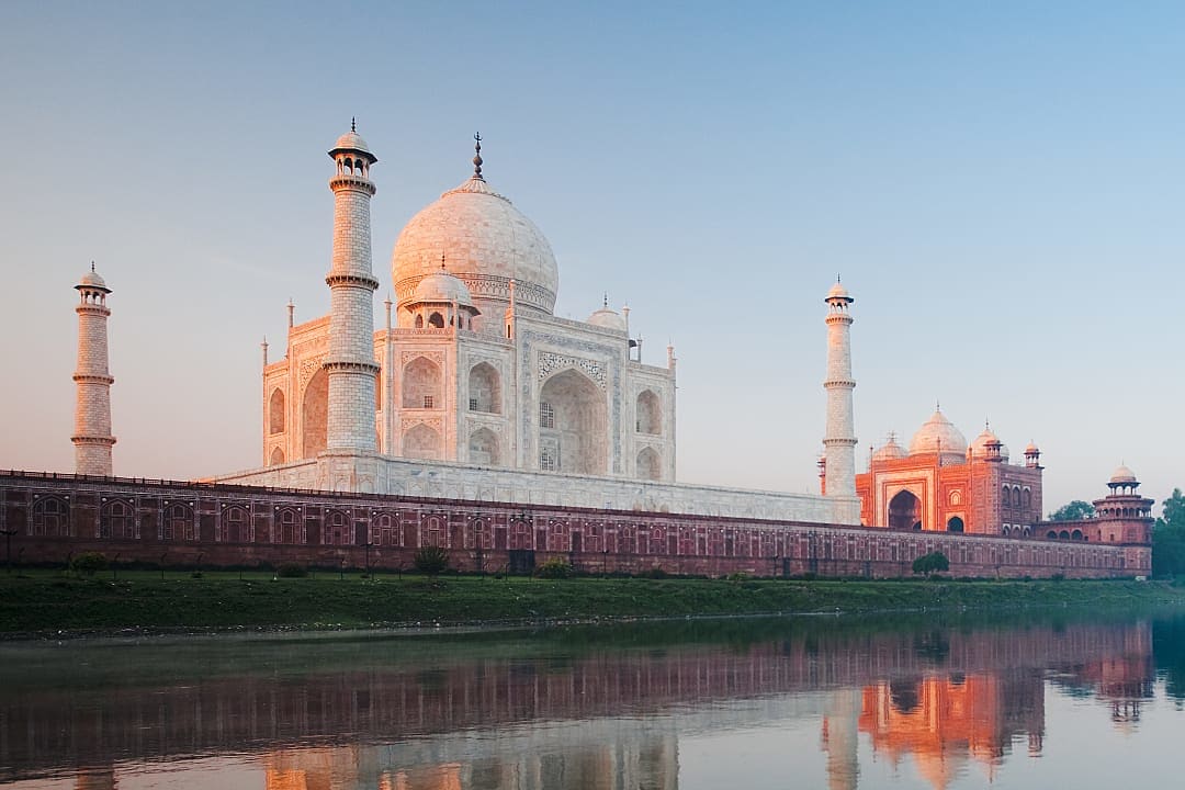 Iconic marble mausoleum reflects in river at peaceful sunrise glow.
