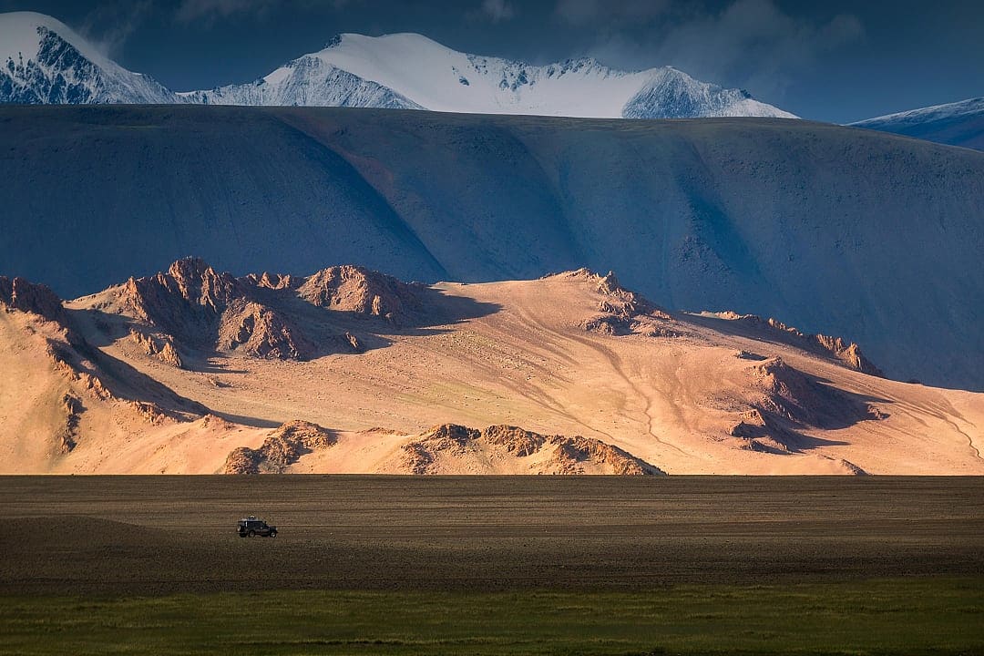 Vehicle crossing the vast plains near Tsambagarav Mountain, a snow-capped peak in Mongolia's Khovd Province region