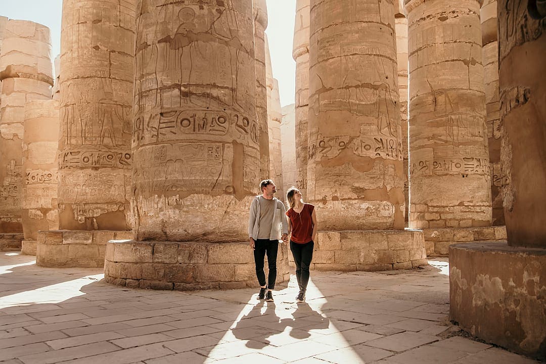 A couple walking between towering ancient stone columns with carved hieroglyphs.