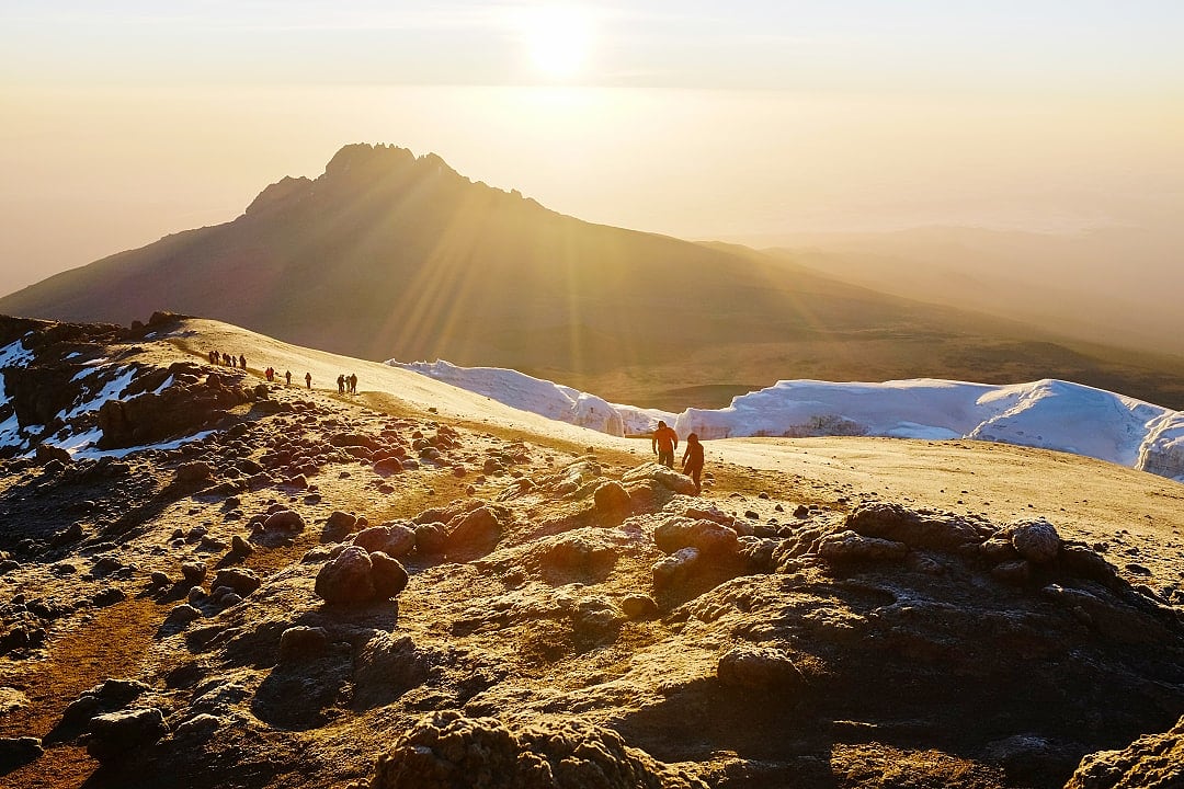 Golden light spills over the summit of Kilimanjaro, as hikers trace the ridgeline.