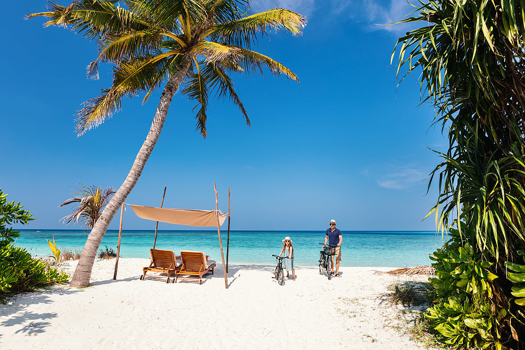 Father and daughter walking their bikes on the beach in the Maldives