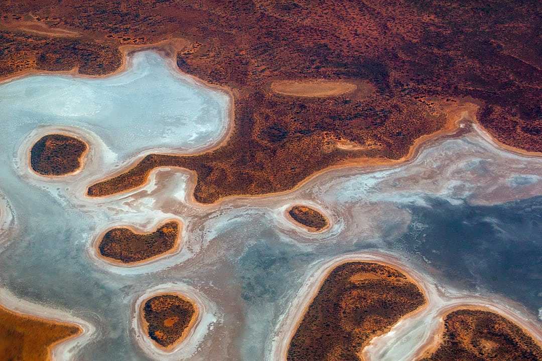 High-altitude aerial view of crystalline salt lakes and ochre-colored desert patterns in Queensland, Australia.