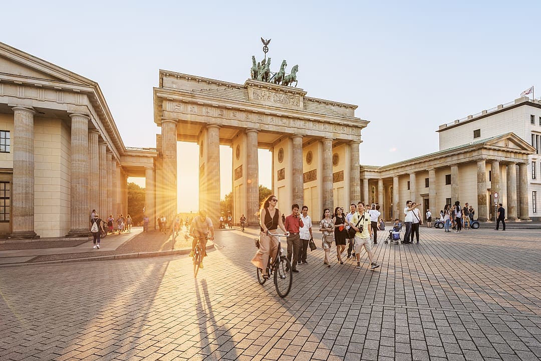 Brandenburg Gate at sunset in Berlin, Germany, with people walking and biking in the historic plaza.