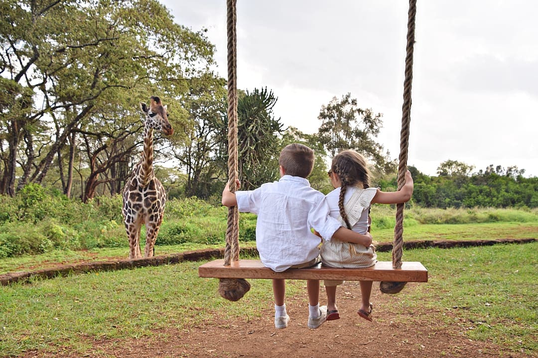 Brother and sister on sitting a tree swing at Giraffe Manor in Nairobi, Kenya