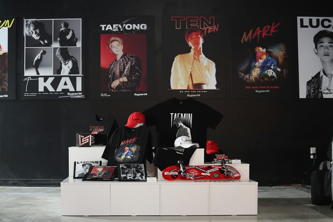 SuperM K-pop merchandise display with posters, T-shirts, hats, and albums