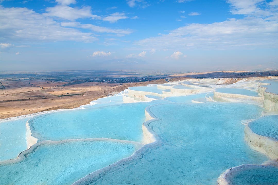 Pamukkale showcases stunning natural beauty and geological wonder, with swirling blue waters cascading over white, icy-like terraces.