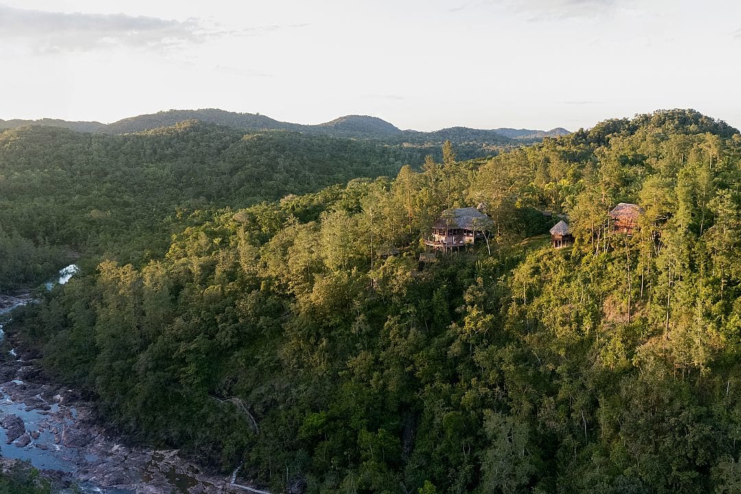 Luxury lodge nestled in lush green jungle hills with a river flowing through a scenic mountain valley