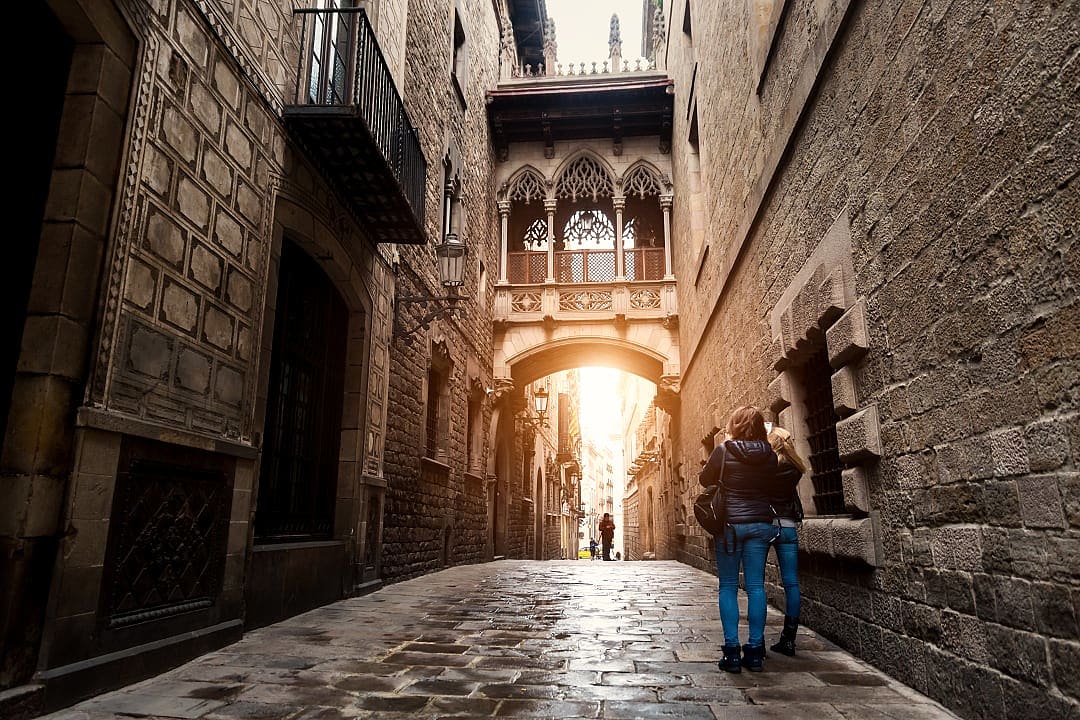Two female travelers dressed for cooler weather taking a photo in the Gothic Quarter of Barcelona