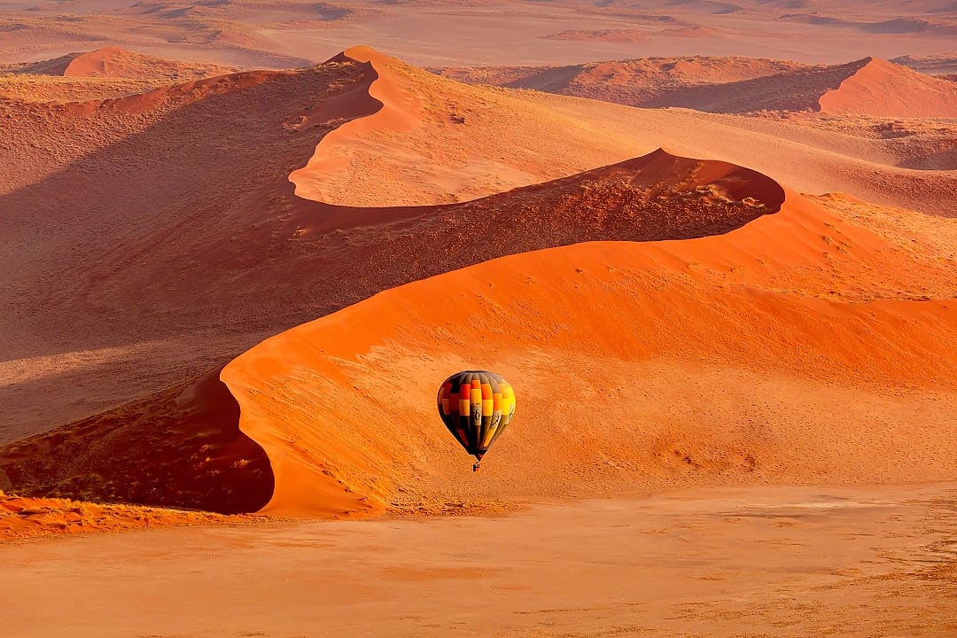 A hot air balloon drifts above Namibia's stunning Sossusvlei dunes.