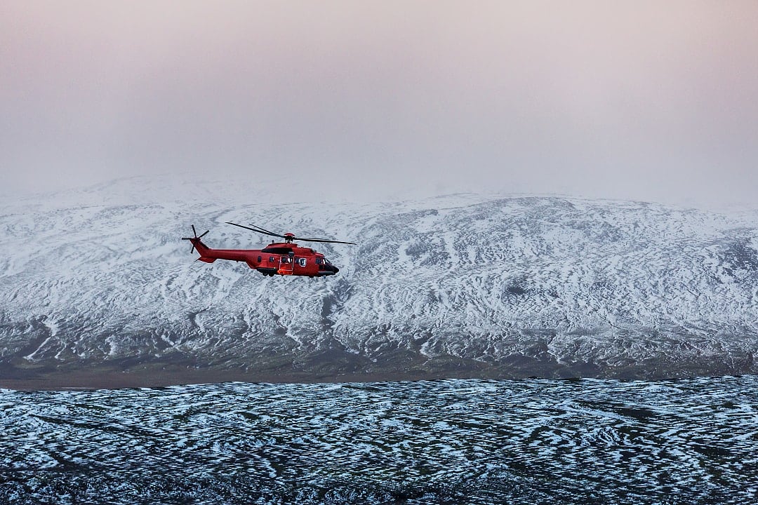Red helicopter flying over a snowy mountain landscape in Iceland.
