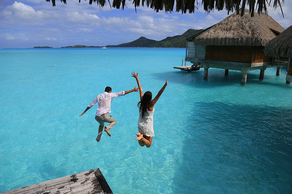 Happy young couple jump into the water from their over water bungalow in Bora Bora