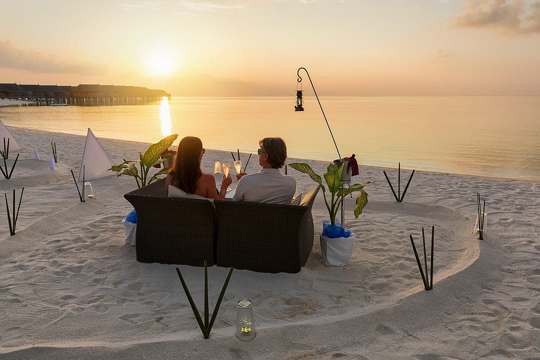 Couple enjoys sunset champagne on serene Maldives beachside setup.