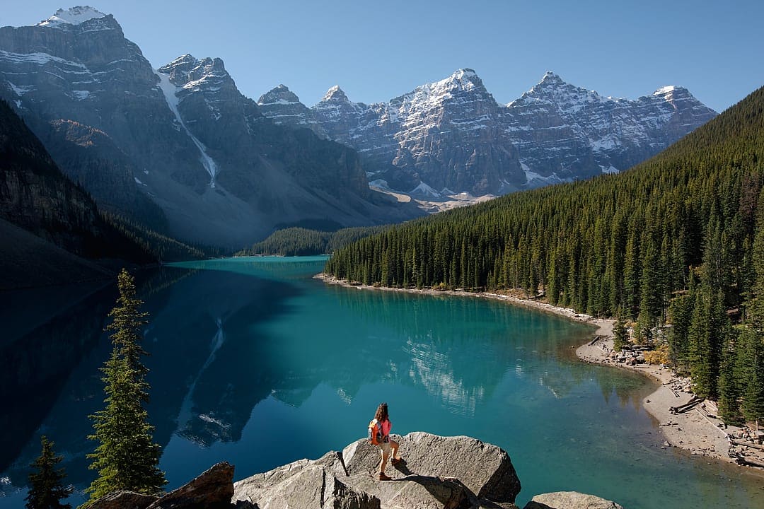 A traveler admires Moraine Lake’s turquoise waters and towering mountains.