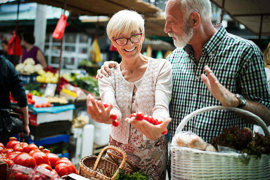 A senior couple smiling while shopping for fresh produce at an outdoor local market.