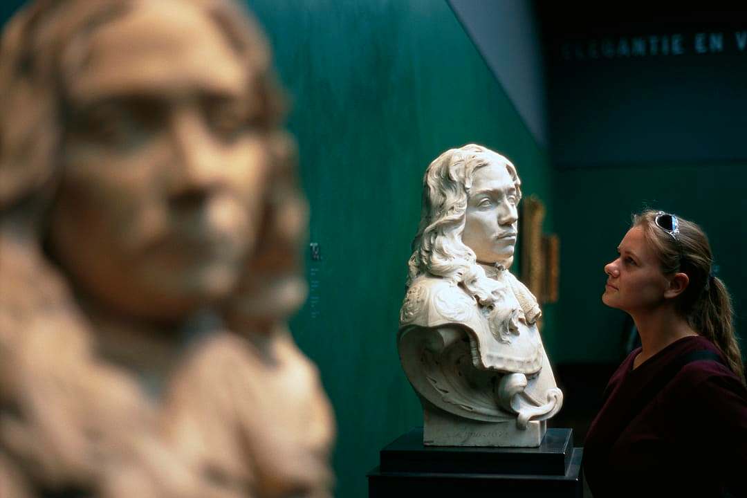 A woman intently observing museum-quality marble bust sculptures in a gallery setting.