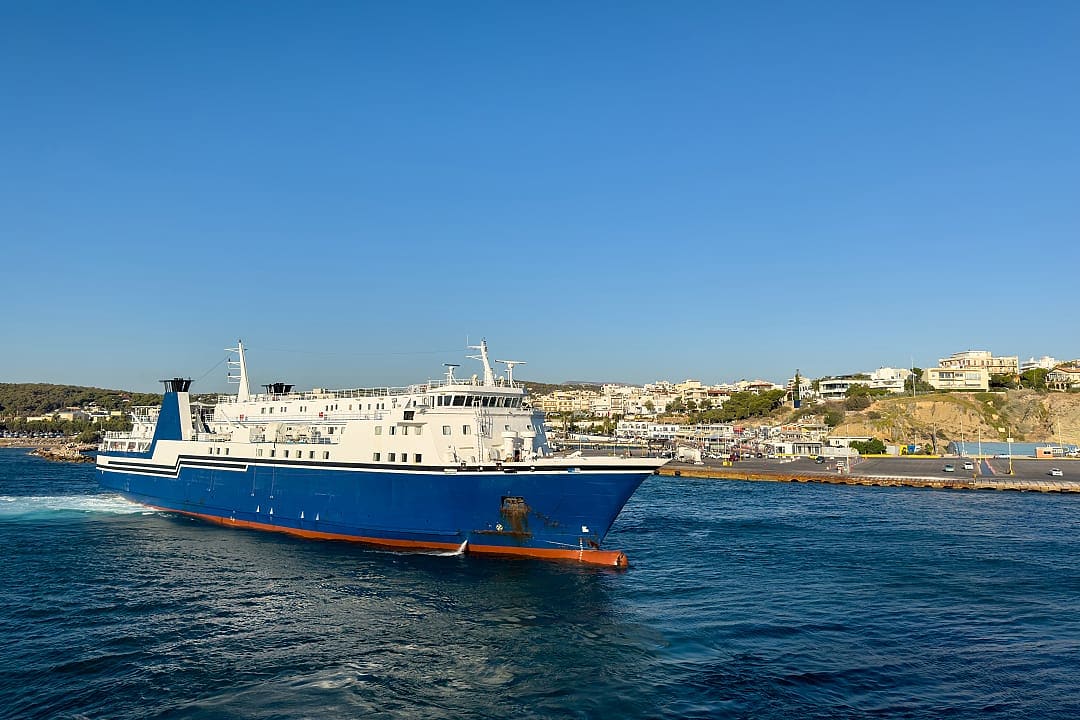 Large blue and white passenger ferry sailing near a coastline.