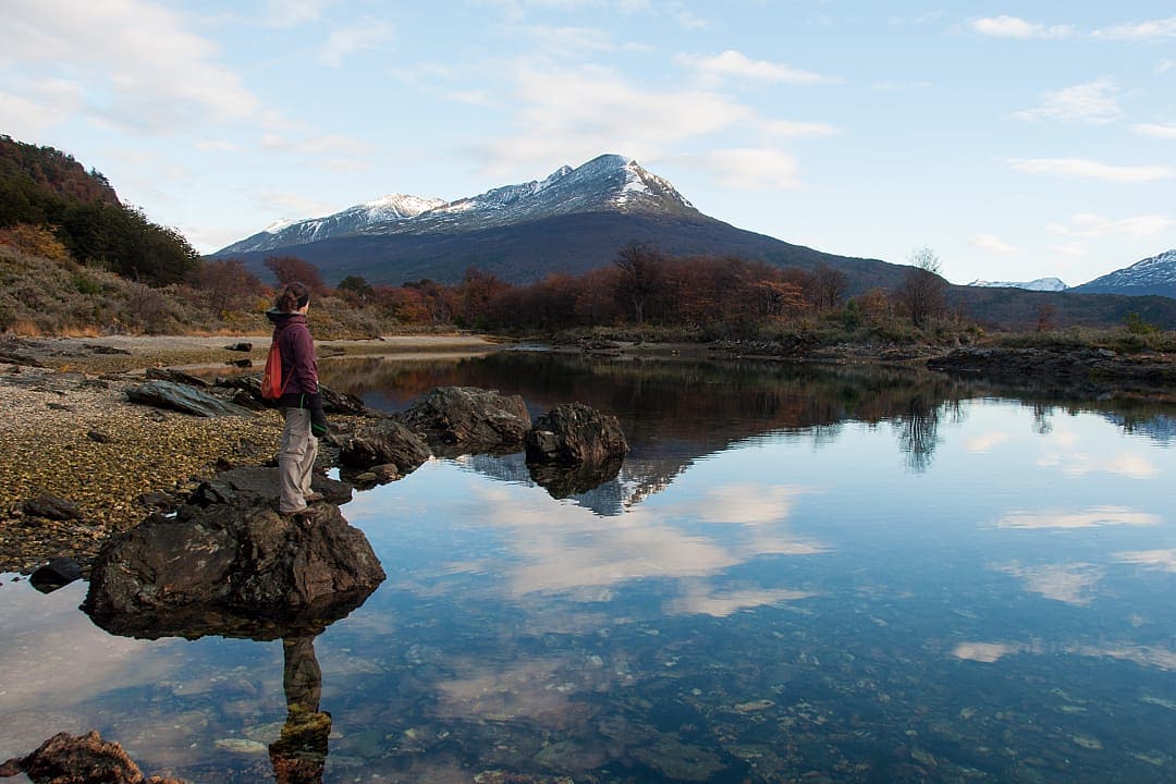 A hiker admires calm waters reflecting mountains in Tierra del Fuego.
