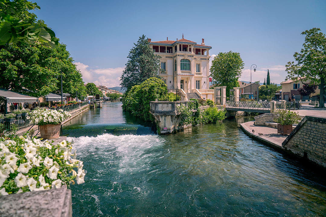 Charming riverside view of L'Isle-sur-la-Sorgue in Provence, France, with historic buildings and bridges.